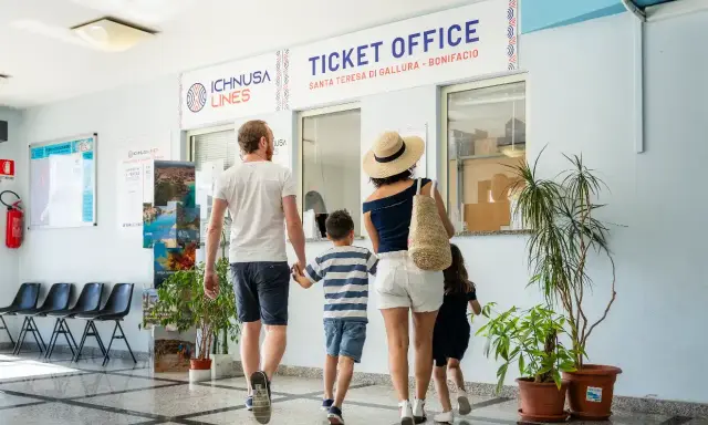 Famiglia in coda all'ufficio biglietti per la Corsica con bambini, pronti per l'avventura.