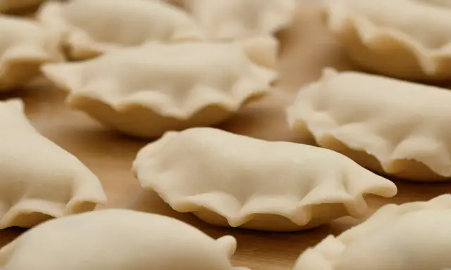 Surowe pierogi z jagodami leżą na drewnianej desce, gotowe do gotowania.