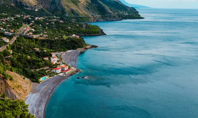 Villaggio costiero con case bianche e rosse affacciato su una spiaggia di ciottoli scuri e mare blu intenso. Le **basilicata spiagge** offrono panorami mozzafiato.