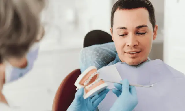Dentysta pokazuje pacjentowi model szczęki z aparatem ortodontycznym, omawiając, czy trzeba usuwać ósemki do aparatu ortodontycznego.