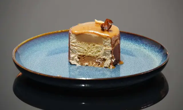 Tranche d'entremet aux couches aériennes, surmontée d'un glaçage caramel et d'une noisette croquante. Le biscuit noisette pour entremet offre une texture légère et savoureuse.