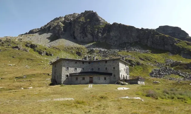 Un imponente rifugio in pietra, incastonato tra prati verdi e rocce imponenti, domina il paesaggio alpino. Un luogo ideale per chi cerca avventura e tranquillità nel cuore della Valle d'Aosta.