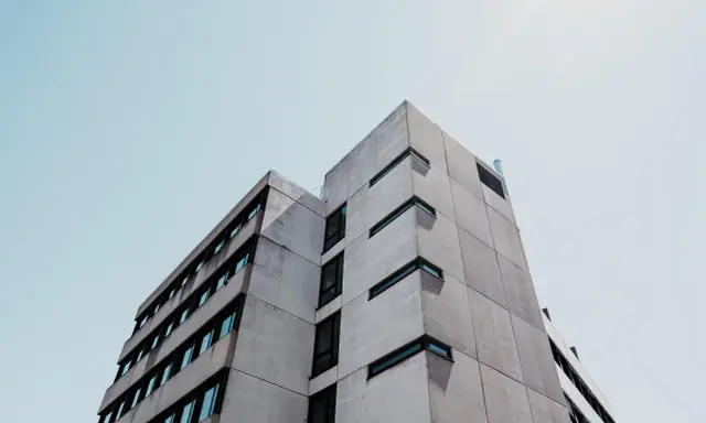 Betonowy budynek o geometrycznej bryle, z rzędami okien. Ta kategoria obiektu budowlanego dominuje w kadrze.