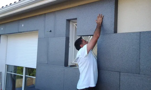 Un ouvrier pose des panneaux d'isolation extérieure en fibre de bois gris.