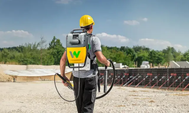 Bauarbeiter mit Rucksackeinheit und Rüttler zur Beton verdichten auf einer Baustelle.
