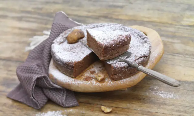 Gâteau au chocolat saupoudré de sucre glace, avec des châtaignes. Une part est coupée, prête à être dégustée. Une recette de châtaigne à essayer !