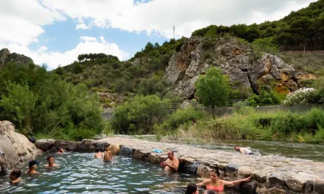 Gente disfrutando de las piscinas naturales en La Rioja, rodeadas de vegetación y rocas.