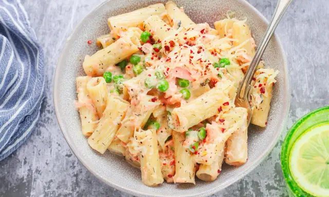 Pyszne danie z makaronem rigatoni, kawałkami łososia, groszkiem i kremowym sosem, posypane serem i płatkami chili. Idealna pasta z łososia na obiad.