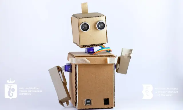 Uroczy robot z kartonu, z oczami-sensorami i kolorowymi kablami, gotowy do nauki i zabawy.