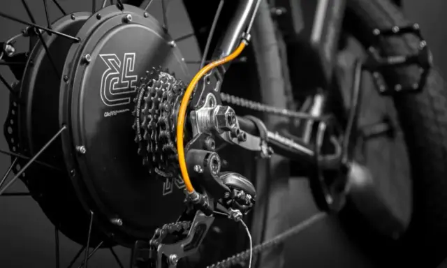 Zestaw do konwersji roweru: czarna piasta z logo, kasetka Shimano, pomarańczowy przewód i przerzutka.