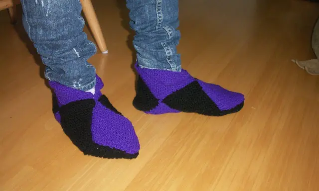 Ett par stickade innetofflor i lila och svart, med jeans till. Perfekta för mysiga hemmakvällar.