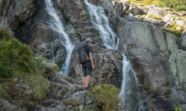 Turysta podziwia wodospad w Tatrach. Wspaniałe widoki, gdzie w Tatry zabierają nas górskie szlaki.