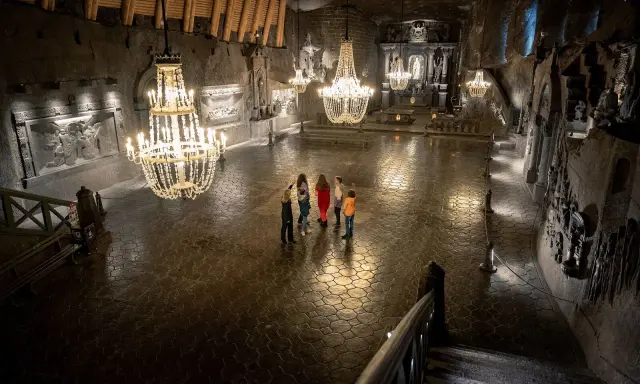 Grupa turystów w podziemnej kaplicy Kopalni Soli w Wieliczce, oświetlonej kryształowymi żyrandolami.