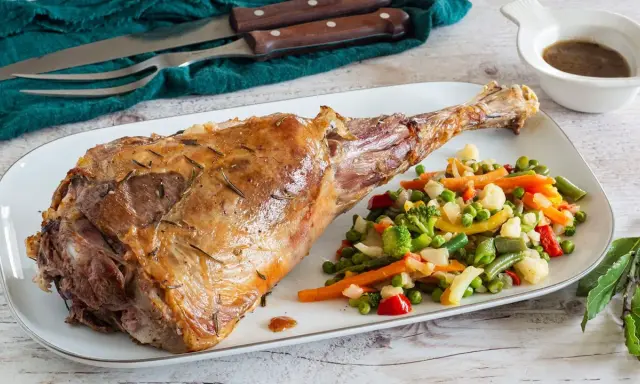 Succulento agnello al forno, dorato e profumato, servito con un contorno di verdure miste colorate.