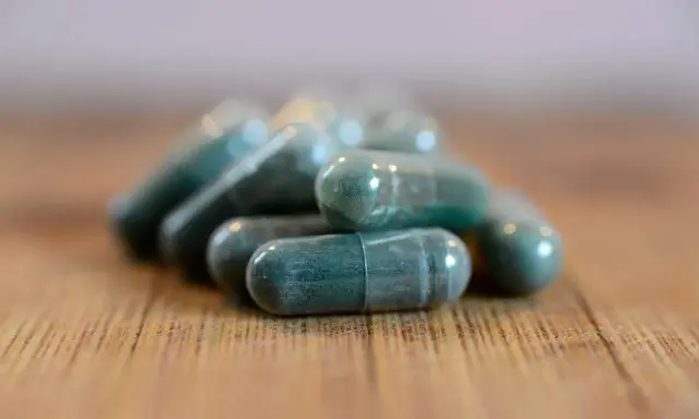 Pile di capsule verdi su un tavolo di legno. Si possono prendere due antibiotici insieme, ma sempre sotto controllo medico.