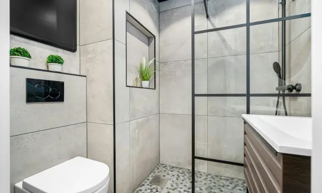 Mampara de ducha con diseño de ventana, separando el espacio de la ducha. Baño moderno con inodoro y lavabo.