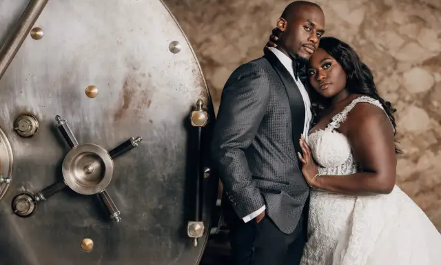 A groom in a patterned tuxedo jacket stands beside a vintage vault door. The father of the bride wears a sharp, dark suit with a satin lapel.
