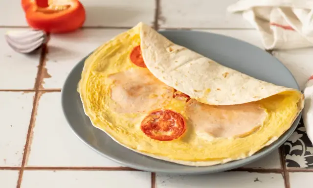 Pyszna tortilla z jajkiem, pomidorkami i szynką, gotowa do zjedzenia.