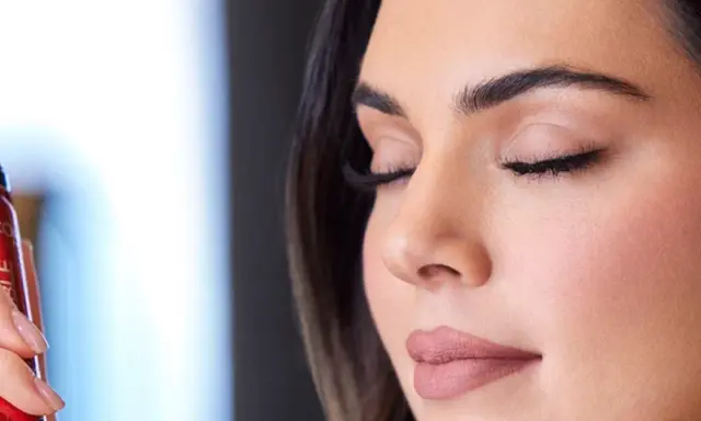 Una mano sostiene un spray fijador de maquillaje rojo. Ideal para cuando usar y mantener tu look perfecto.