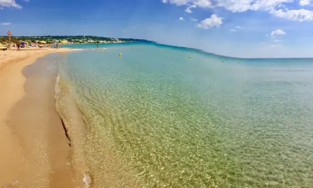 Spiaggia delle Maldive in Puglia: sabbia dorata, acque cristalline e un cielo azzurro con nuvole bianche. Un paradiso terrestre.