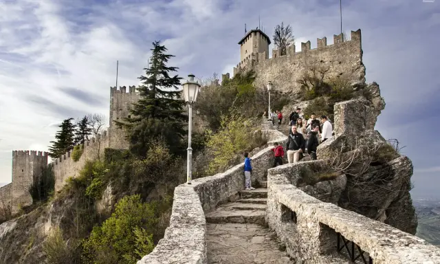 Sentiero roccioso verso le torri di San Marino, un viaggio nella storia. Turisti salgono la scalinata che porta alle antiche fortificazioni.