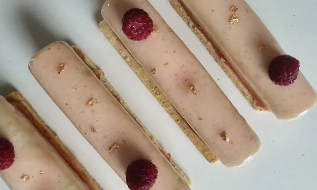 Quatre délicieux rectangles de crème chiboust ou diplomate, ornés de framboises fraîches et de feuilles d'or comestibles.
