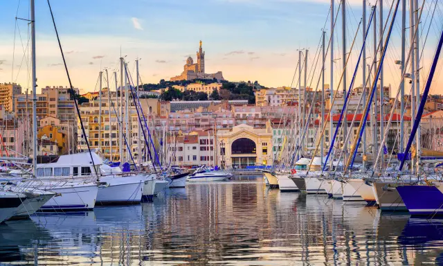 Barche a vela ormeggiate nel porto di Marsiglia, con la Basilica di Notre-Dame de la Garde sullo sfondo. Un'ottima vista per chi cerca cosa vedere a Marsiglia vicino al porto.