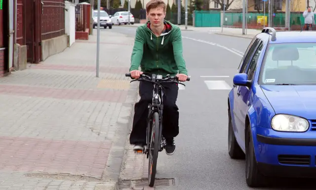 Młody mężczyzna na rowerze jedzie po chodniku, obok drogi. To miejsce, gdzie można jeździć bez karty rowerowej.