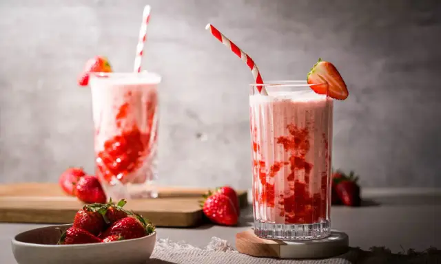 Zwei Gläser mit einem cremigen Erdbeer Milchshake, garniert mit frischen Erdbeeren und gestreiften Strohhalmen.