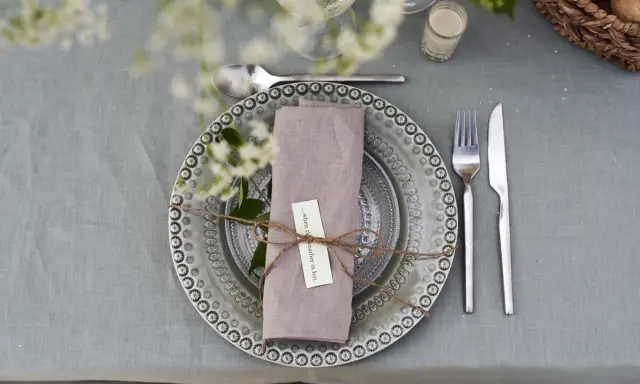 Vacker dukning med linneservetter, blommor och en korg med bröd. Perfekt för en sommarfest.