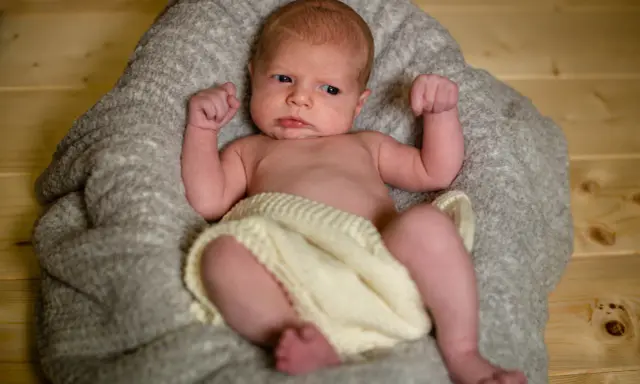 Un neonato con un'espressione curiosa, avvolto in una coperta, pronto per un servizio fotografico flash neonati.