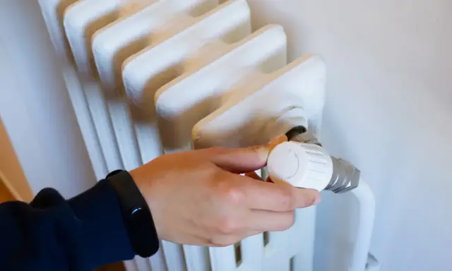 Mano ajustando el termostato de un radiador blanco. Controlar la temperatura ayuda a saber cuanto cuesta la calefaccion al mes.