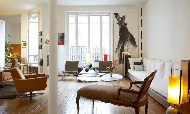 Un salon lumineux où les meubles anciens reviennent à la mode, avec un fauteuil vintage, une méridienne et une grande œuvre d'art.