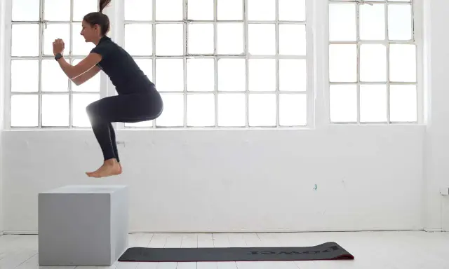 Frau macht **box jumps** in einem hellen Raum mit großen Fenstern.