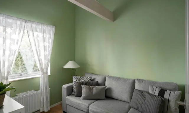 Sofá gris con cojines, lámpara y cortinas blancas junto a pared verde. ¡Excelentes ideas pintar casa con este tono fresco!