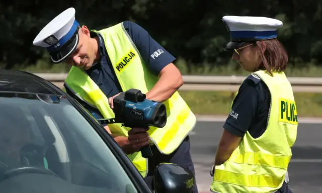 Policjanci w kamizelkach odblaskowych mierzą prędkość samochodu radarem.