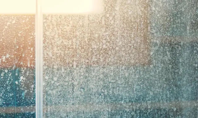 Gouttes d'eau et traces de calcaire sur une vitre de douche, créant un motif abstrait et flouté.