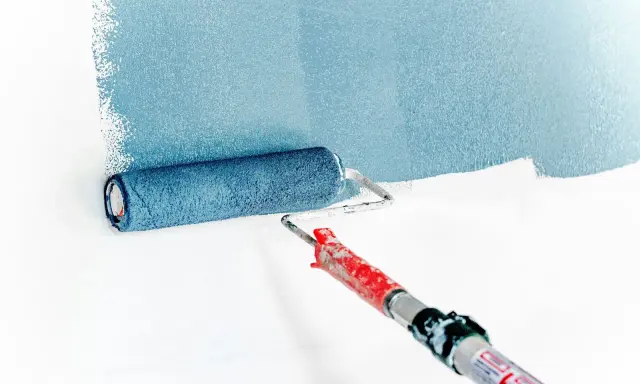 Rodillo aplicando pintura azul sobre pared blanca. La imprimación es el primer paso para un acabado perfecto.