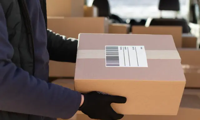 Kurier w czarnej rękawiczce trzyma paczkę z etykietą DPD. To pokazuje, ile jest ważna etykieta DPD dla sprawnej dostawy.