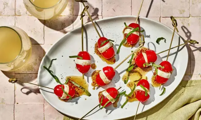 Szybkie przekąski na ognisko: pomidorki koktajlowe z mozzarellą i bazylią na patyczkach, polane sosem.