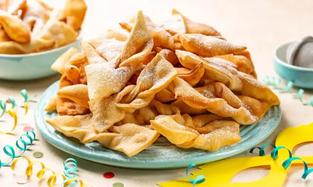 Un piatto colmo di chiacchiere, dolci tipici di Carnevale, cosparse di zucchero a velo. Festa e gusto, ecco cosa si mangia a Carnevale!