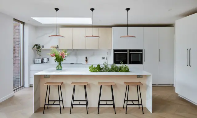 Cuisine moderne avec îlot central, tabourets en bois et une niche ouverte intégrée dans les placards.