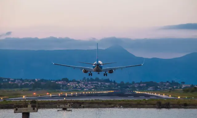 Ett flygplan landar vid Korfu flygplats i skymningen. Landningsbanans ljus lyser upp vägen.