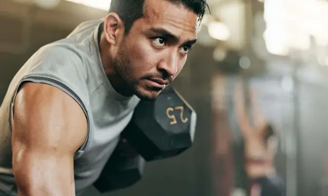 Fokusierter Mann hebt Hantel. Sein Schweiß glänzt. Ein Teil eines 2er Split Trainingsplans.