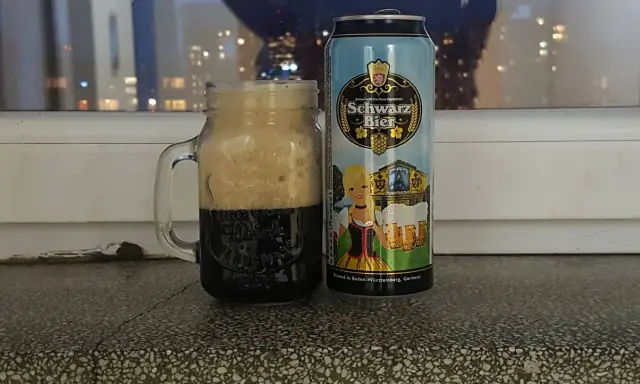 Perlenbacher Schwarz Bier w kuflu, obok puszka piwa. Wieczorny widok na miasto w tle.