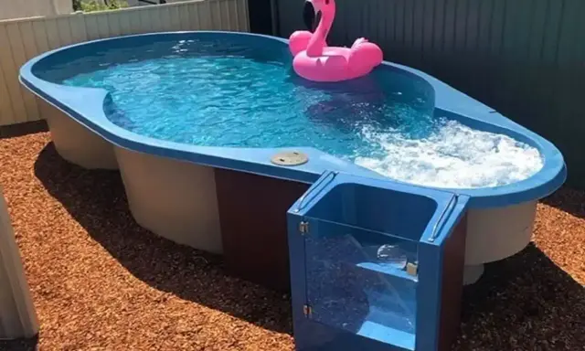 Petit jardin avec aménagement abord piscine hors sol. Un flamant rose gonflable flotte sur l'eau bleue.