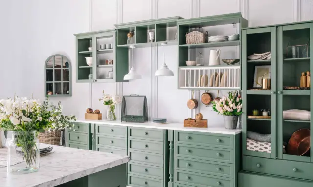 Cucina in stile provenzale casa con mobili verdi, pentole in rame appese e fiori freschi.