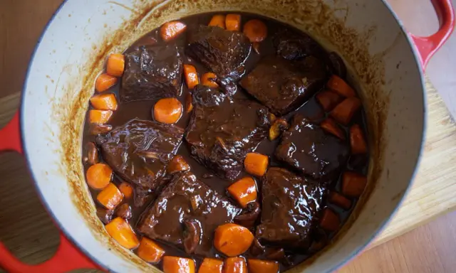 Boeuf bourguignon casero en olla roja, con trozos de carne tierna, zanahorias y champiñones en una rica salsa.