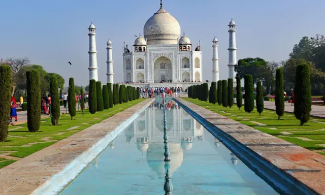 Majestatyczny Taj Mahal w Indiach odbija się w spokojnej wodzie, otoczony zielonymi ogrodami i strzelistymi cyprysami.