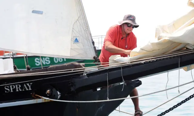 Un homme, Guy Bernardin, ajuste les voiles du Spray, un voilier historique, par une journée ensoleillée.